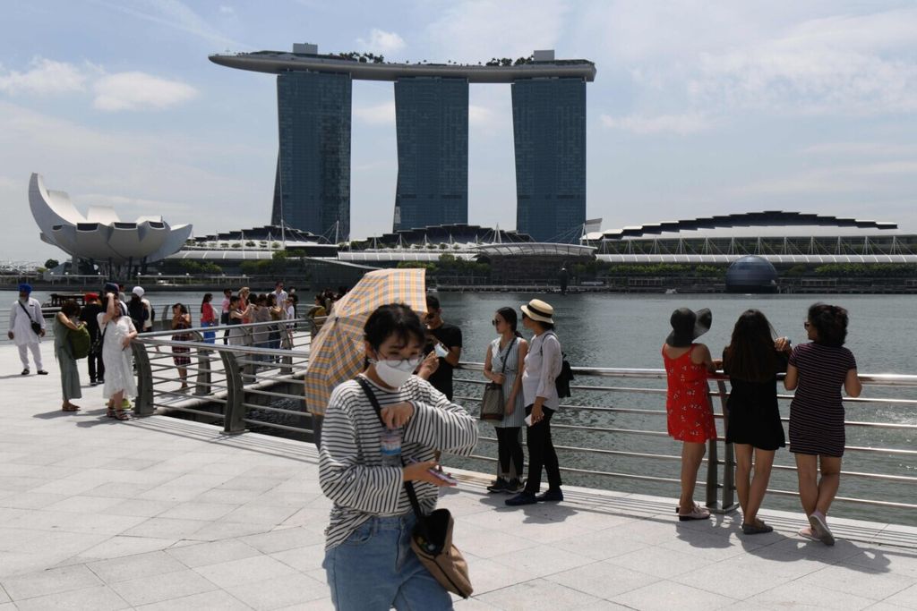 Wisatawan di Singapura yang menggunakan masker untuk mencegah terjangkit Covid-19 berjalan di kawasan Merlion Park, Senin (17/2/2020).