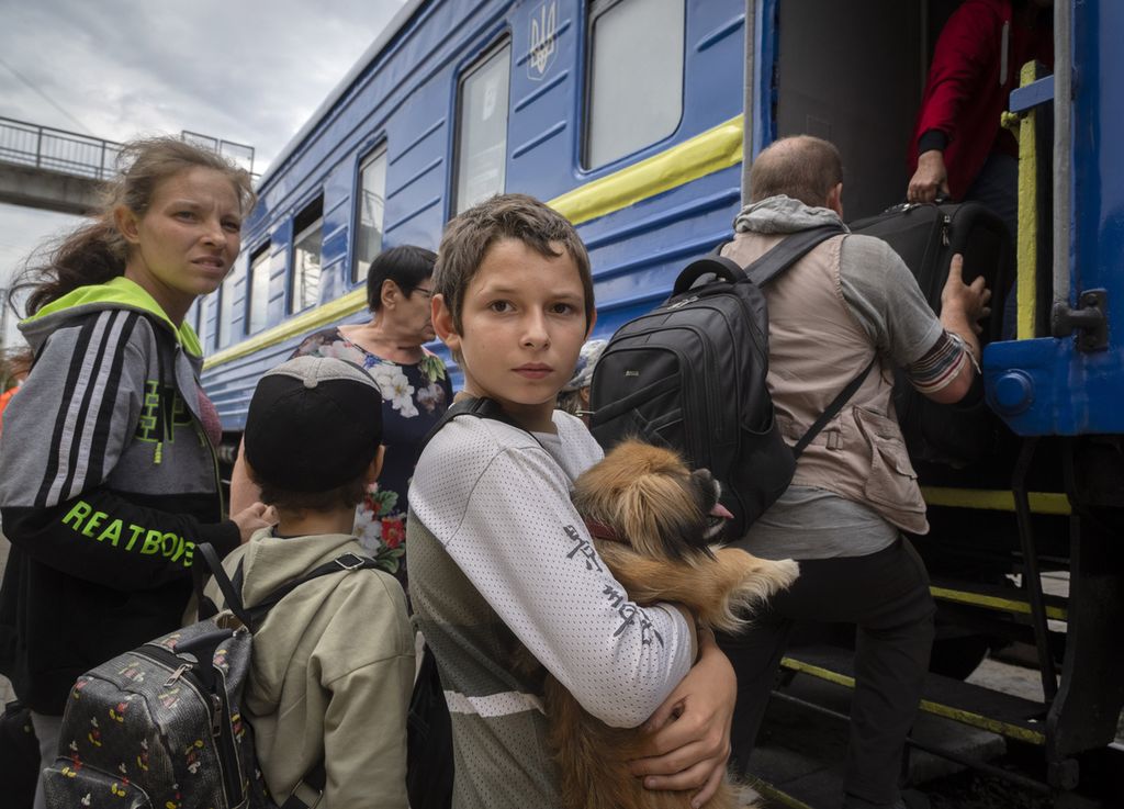Seorang anak menggendong anjing saat ia dan keluarganya dievakuasi dari area pertempuran dengan kereta di Pokrovsk, Ukraina timur, Sabtu (25/6/2022). 