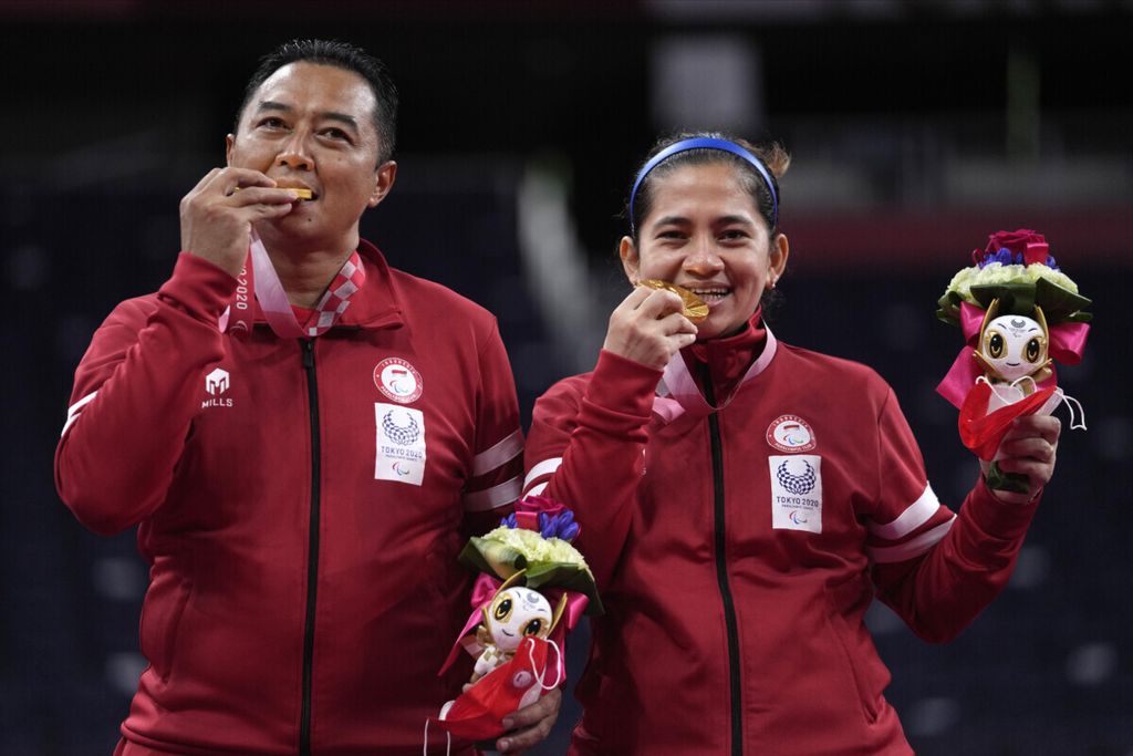 Ganda bulu tangkis Indonesia, Hary Susanto (kiri) dan Leani Ratri Oktila, menggigit medali emas yang diraih mereka seusai memenangi final ganda campuran klasifikasi SL3-SU5 Paralimpiade Tokyo 2020, Minggu (5/9/2021). Mereka mengalahkan ganda Perancis, Lucas Mazur/Faustine Noel, 23-21, 21-17. 