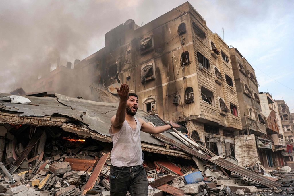Seorang pria berdiri di dekat bangunan runtuh dan terbakar akibat gempuran Israel di kota Gaza, 11 Oktober 2023. 
