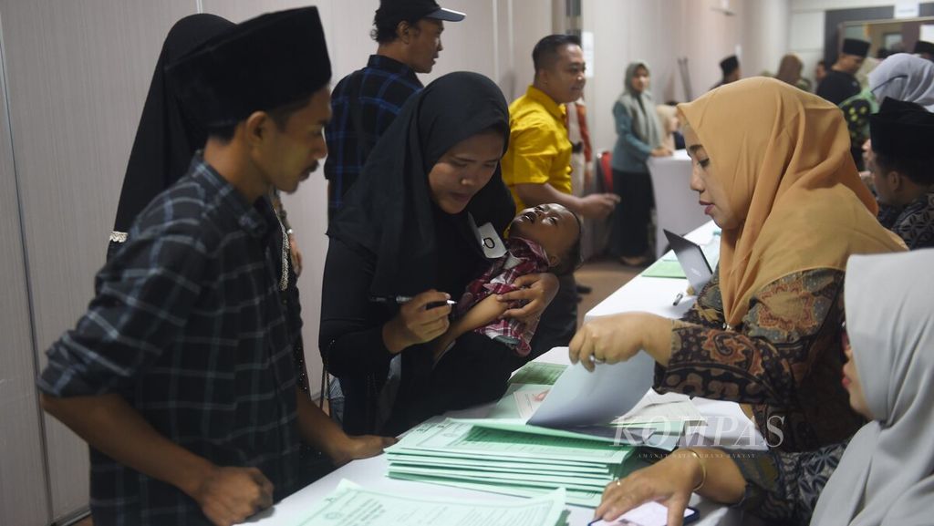 Dengan menggendong anaknya, seorang peserta nikah massal menandatangani berkas seusai mengikuti sidang isbat pernikahan di Gedung Siola, Surabaya, Selasa (2/7/2024). 