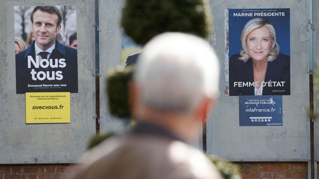 Seorang pria berjalan melewati poster kampanye kandidat presiden Prancis, petahana Emmanuel Macron (kiri) dan kandidat presiden partai sayap kanan Rassemblement National (RN) Perancis, Marine Le Pen, di Denain, 11 April 2022. 