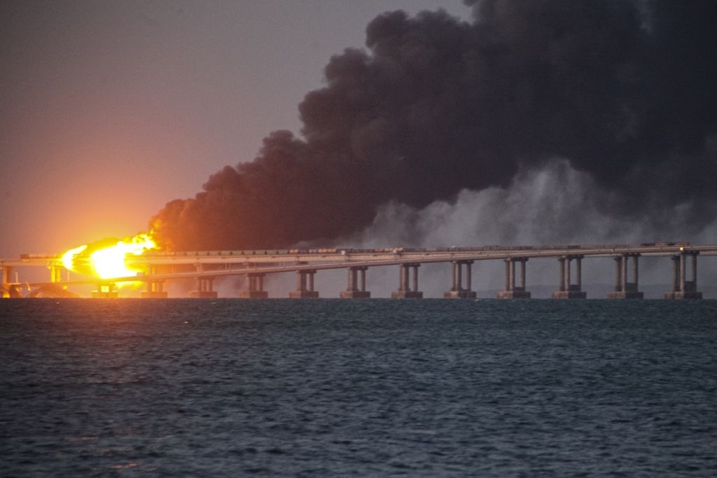 Kobaran api dan asap hitam membubung dari Jembatan Kerch, penghubung wilayah Rusia dengan Semenanjung Crimea, Sabtu (8/10/2022). Pemerintah Rusia menyatakan, bom yang dibawa truk meledakkan jembatan. Tiga orang dilaporkan tewas. 