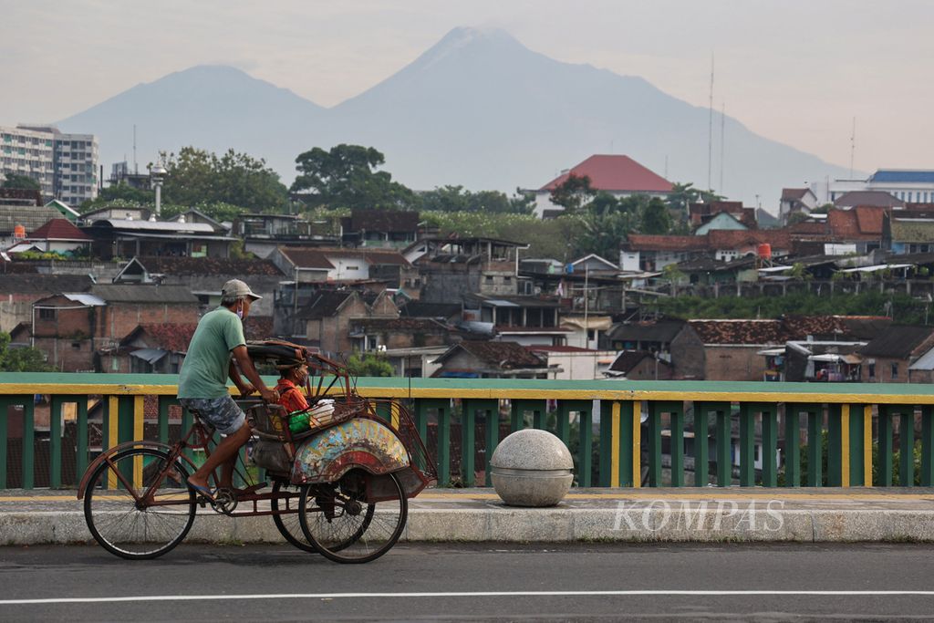 Pengguna becak melintas di Jembatan Gondolayu, Yogyakarta, dengan latar belakang pemandangan Gunung Merapi, Jumat (11/3/2022) pagi. 