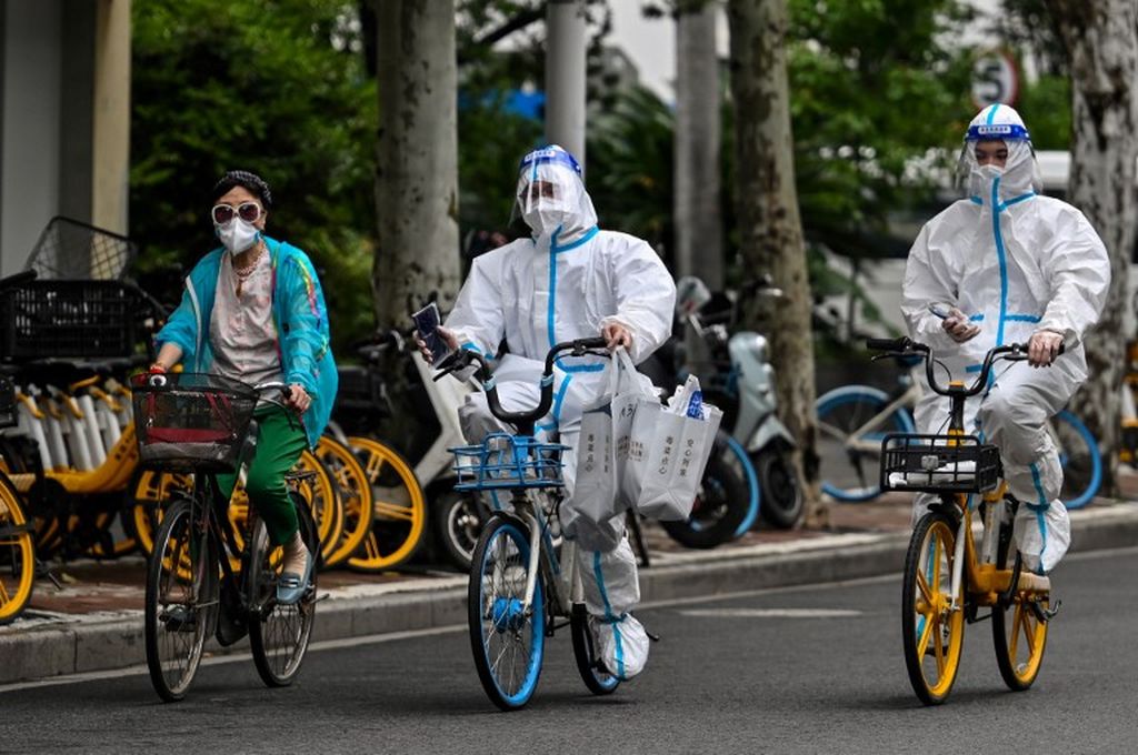 Para pekerja dengan memakai alat pelindung diri bersepeda di sebuah ruas jalan saat berlangsung penguncian wilayah guna meredam persebaran wabah Covid-19 di Distrik Jing'an, Shanghai,  China, 29 Mei 2022.