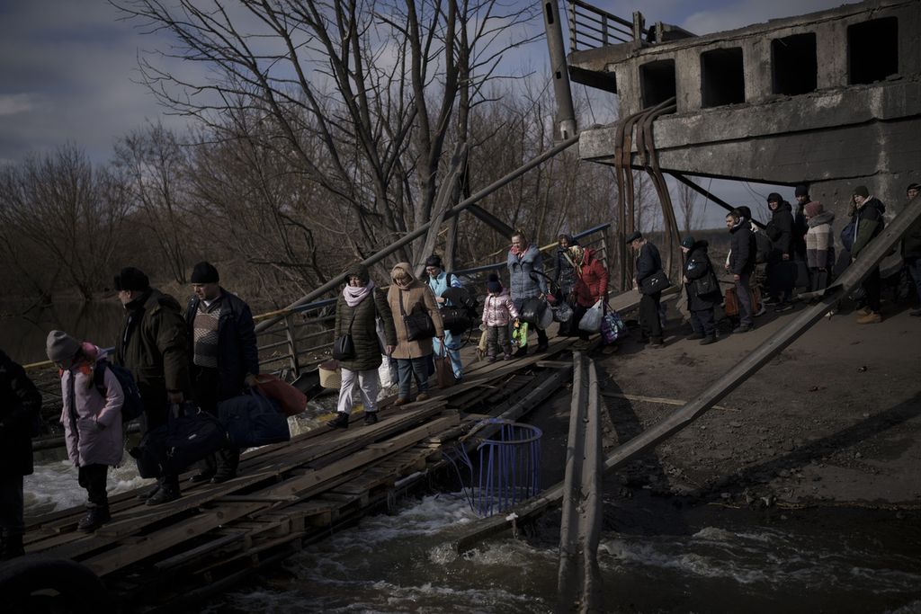 Warga Ukraina melintasi jalur darurat di bawah jembatan yang hancur saat melarikan diri dari Irpin, di pinggiran Kiev, Ukraina, Rabu (9/3/2022).