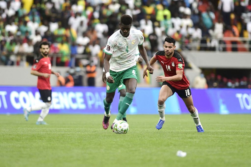 Pemain Senegal, Pape Abou Cise (kiri), dikejar pemain Mesir, Nabil Dounga, saat pertandingan babak ketiga <i>leg </i>kedua kualifikasi Piala Dunia 2022 antara Senegal dan Mesir di Stadion Abdoulaye Wade, Dakar, Senegal, Rabu (30/3/2022) dini hari WIB. Senegal lolos ke Piala Dunia 2022 setelah mengalahkan Mesir melalui adu penalti, 3-1. 