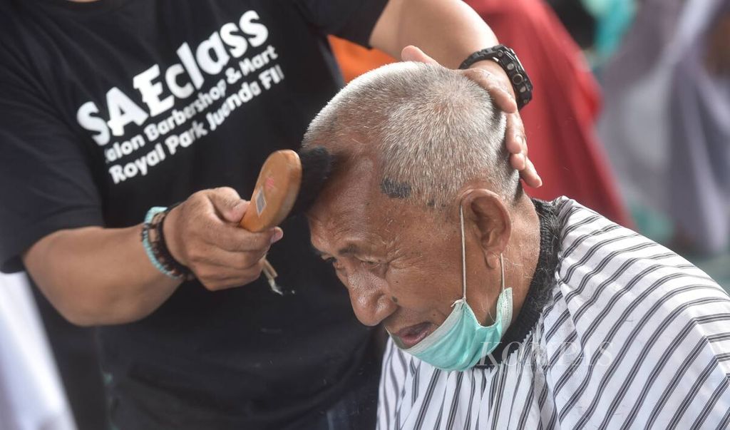 Sukarelawan membersihkan kepala warga dari rambut yang telah dipotong saat kegiatan potong rambut gratis di halaman Masjid Muhammad Cheng Hoo, Kota Surabaya, Jawa Timur, Senin (18/4/2022). 