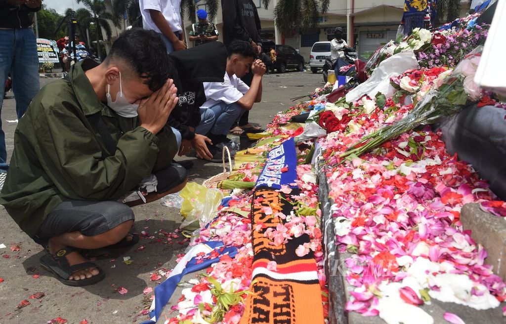 Suporter yang berada di Patung Singa Tegar di kawasan Stadion Kanjuruhan, Kabupaten Malang, Jawa Timur, memanjatkan doa bagi rekan mereka yang meninggal saat kerusuhan, Senin (3/10/2022). 