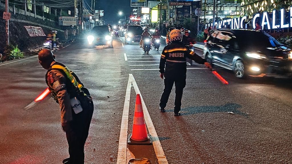 Dua petugas Satlantas Polres Bogor mengarahkan kendaraan yang turun dari arah Puncak menuju Gadog-Jakarta, Sabtu (13/4/2024). Pemberlakuan sistem satu arah berlangsung dari pukul 10.45 hingga pukul 23.00 atau selama 12 jam.