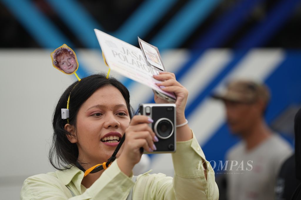Fotografer memanfaatkan kamera polaroid memotret penggemar bintang pop asal Inggris, Edward Christopher Sheeran alias Ed Sheeran, dalam konser di luar Jakarta International Stadium (JIS), Jakarta, Sabtu (2/3/2024) malam. Satu cetakan foto dijual Rp 20.000.