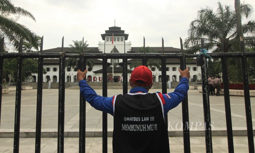 Seorang buruh peserta unjuk rasa memegang pagar Gedung Sate, Kota Bandung, Jawa Barat, Kamis (25/11/2021). Buruh menolak Undang-Undang Cipta Kerja dan menuntut kenaikan upah minimum 2022.