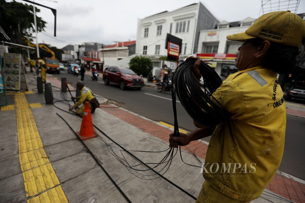 Petugas Dinas Bina Marga mengumpulkan kabel fiber optik hasil pembersihan ke atas truk di kawasan Tebet, Jakarta, Selasa (3/1/2023).