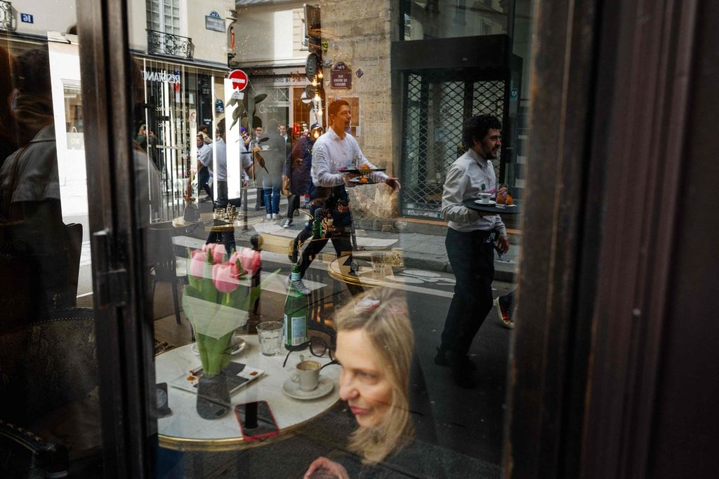 Para pramusaji yang mengikuti perlombaan tradisional Course des Cafes atau perlombaan kafe, Minggu (24/3/2024), di Paris, Perancis, terlihat dari kaca jendela sebuah kafe. 