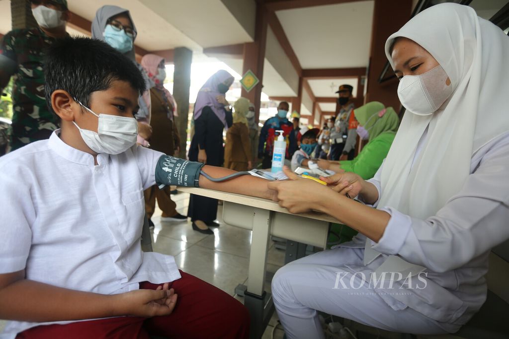 Tenaga kesehatan melakukan pemeriksaan kesehatan kepada siswa sebelum menerima suntikan vaksin Covid-19 di SDN 02 Pondok Bambu, Jakarta Timur, Selasa (14/12/2021). 