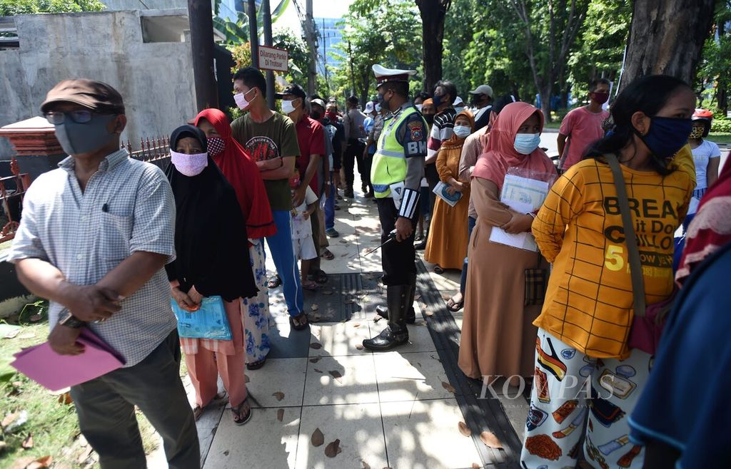 Petugas kepolisian mengatur warga yang akan mencairkan dana bantuan sosial tunai dari Kementerian Sosial di Kantor Pos Jalan Perak Barat, Surabaya, Jawa Timur, Selasa (12/5/2020). Akibat keterbatasan tempat dan diberlakukannya protokol Covid-19, warga banyak yang menunggu nomor antrean di luar Kantor Pos. 