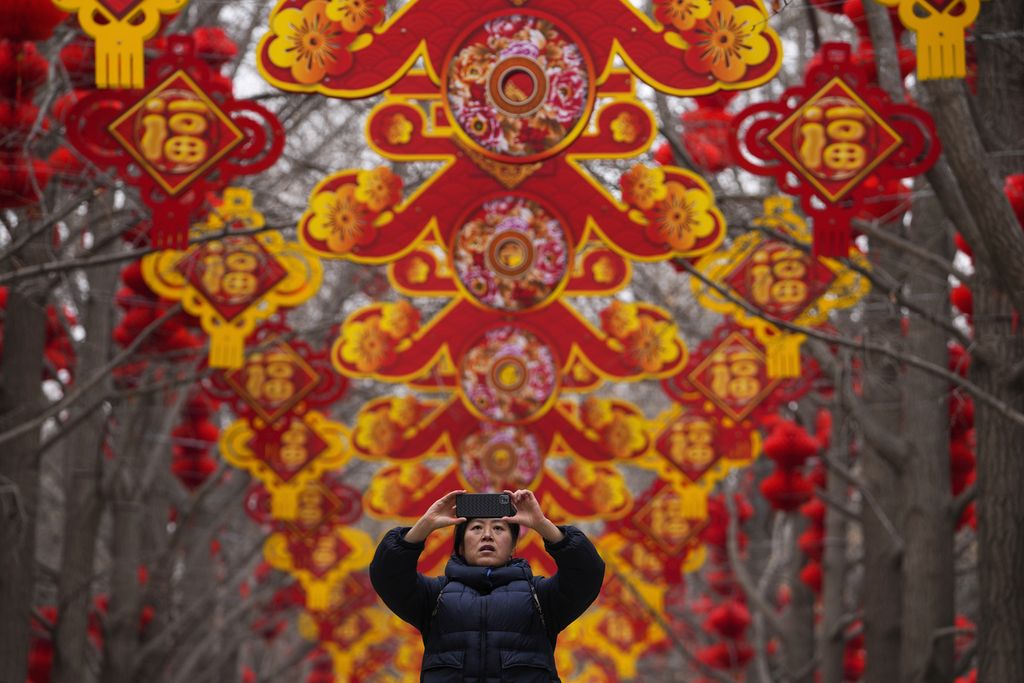 Seorang warga memotret dekorasi lentera merah yang dipasang di pohon di Taman Ditan, Beijing, China, untuk menyambut Tahun Baru China, Minggu, (4/2/2024). 