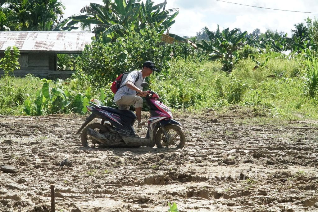 Warga mendorong sepeda motor di Jalan Trans-Mentawai yang masih berlumpur di Desa Madobag, Kecamatan Siberut Selatan, Kepulauan Mentawai, Sumatera Barat, Minggu (31/7/2022). Hingga Oktober 2022, progres pembangunan jalan yang dimulai sejak 2012 ini baru 37,59 persen.