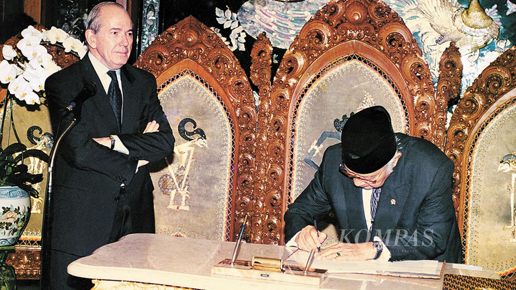 Dengan gaya menggurui, Direktur Pelaksana Dana Moneter Internasional (IMF) Michel Camdessus menyaksikan Presiden Soeharto menandatangani nota kesepakatan bantuan IMF. Peristiwa bersejarah ini terjadi di ruang tengah kediaman pribadi Presiden Soeharto di Jalan Cendana, 15 Januari 1998.