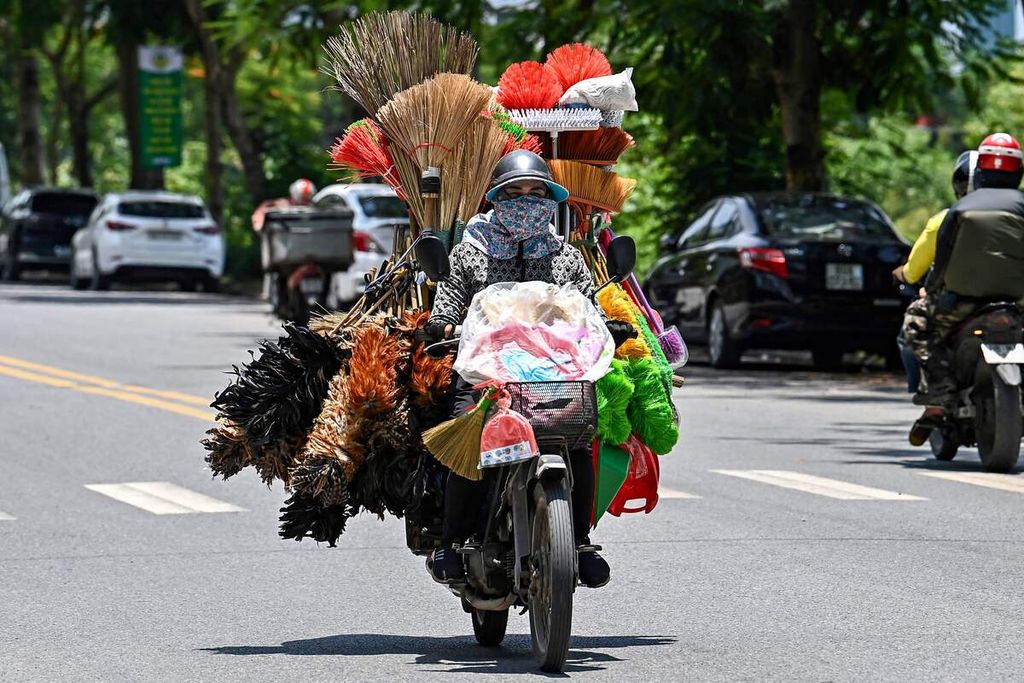 Seorang pedagang keliling tengah membawa beragam alat rumah tangga dengan menggunakan sepeda motor. Foto diambil di Hanoi pada Senin (17/6/2024).