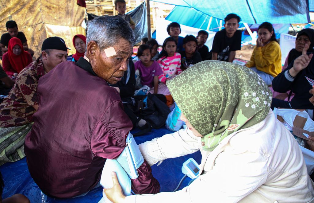 Tenaga medis memeriksa Solihin (70) yang sakit di tenda pengungsian di Kampung Ciberem, Desa Cikanyere, Kecamatan Sukaresmi, Kabupaten Cianjur, Jawa Barat, Minggu (27/11/2022).