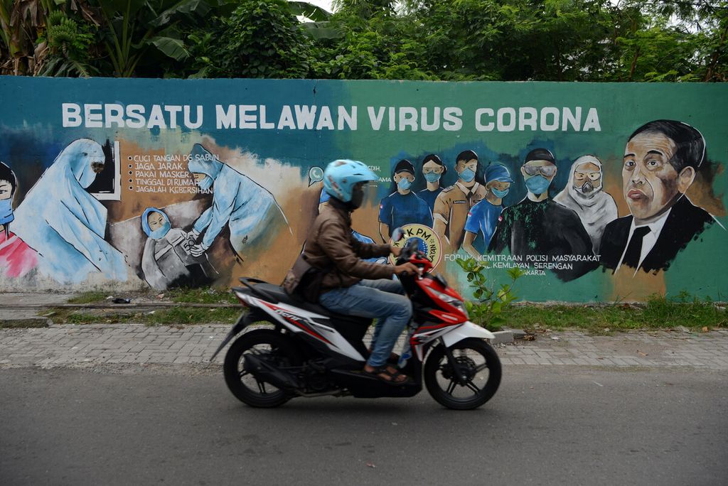 Pesepeda motor melintas di depan mural bertema ajakan bersatu melawan pandemi Covid-19 di Kampung Kemlayan, Serengan, Solo, Jawa Tengah, Selasa (21/4/2020). 