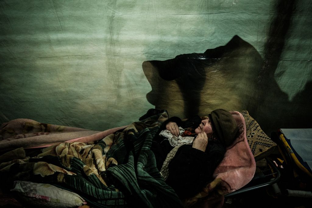 Seorang pengungsi Ukraina berusia 92 tahun berbaring saat menanti petugas Palang Merah Ukraina untuk mengevakuasi dirinya di sebuah bungker di Sievierodonetsk, Ukraina timur, 22 April 2022, di tengah pertempuran di wilayah Donbas. Foto ini merupakan satu dari 100 foto yang dirilis AFP untuk menandai 100 hari invasi Rusia ke Ukraina. 