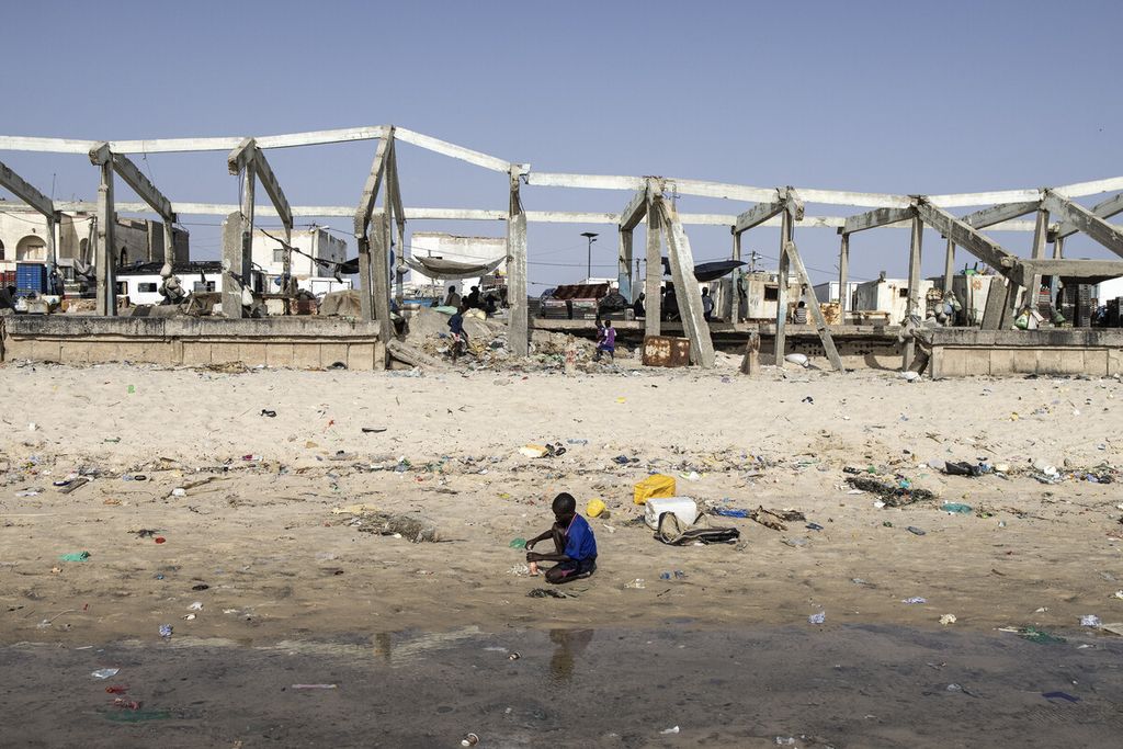 Anak laki-laki duduk di depan reruntuhan pasar ikan di lingkungan nelayan tepi laut Guet NDar di Saint Louis, Senegal, di mana kenaikan permukaan laut telah menggusur ratusan orang-orang dari desa nelayan Guet N Dar ke kamp relokasi, Rabu (11/8/2021). 