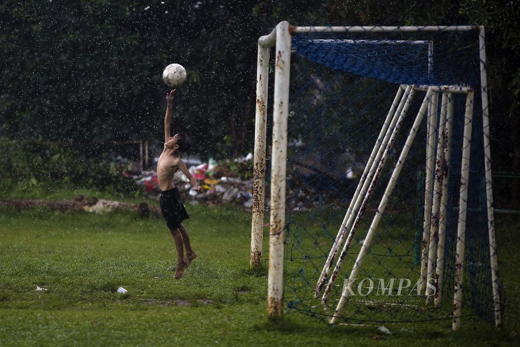 Anak bermain sepak bola di Lapangan Kostrad, Petukangan Utara, Jakarta, saat hujan deras, Senin (25/1/2021). 