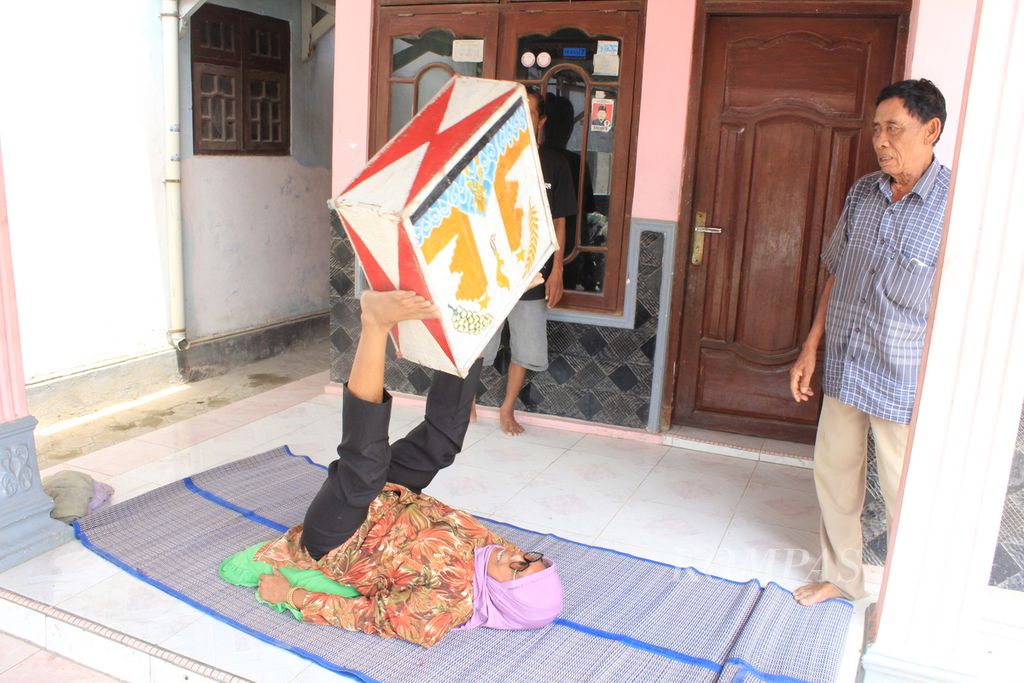  Karsinih (60) mengangkat dan memutar sebuah kotak dengan kedua kakinya saat mencontohkan bagian pertunjukan genjring akrobat di Desa Bayalangu Kidul, Kecamatan Gegesik, Kabupaten Cirebon, Jawa Barat, Minggu (17/9/2023).