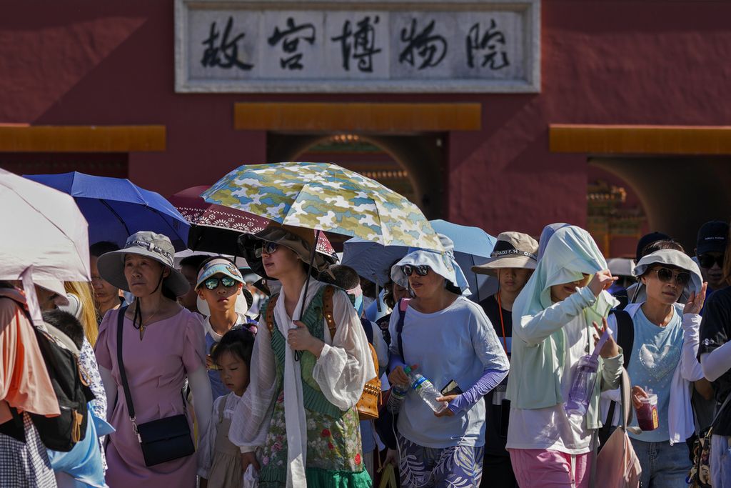Pengunjung mengenakan topi penahan matahari dan membawa payung saat meninggalkan Kota Terlarang pada hari terpanas di Beijing, 29 Juni 2023. 