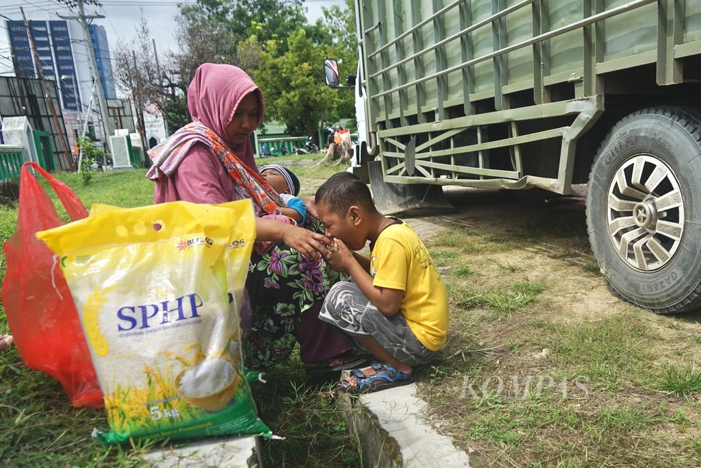 Munirah (40) bersama dua anaknya, Zein (6) dan Rayyan (4 bulan), seusai mengantre beras murah di Kendari, Sulawesi Tenggara, Selasa (27/2/2024). Harga beras di Kendari dan wilayah lainnya terus melonjak. Kenaikan tertinggi terjadi di Wakatobi yang mencapai Rp 1 juta untuk 50 kilogram. 