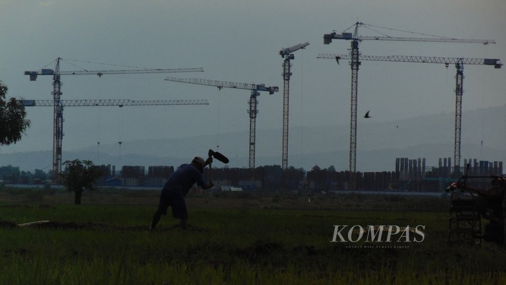 Petani sedang menggarap lahan persawahan di daerah dengan latar pembangunan terminal Bandara Internasional Jawa Barat di Kecamatan Kertajati, Kabupaten Majalengka, Jabar, beberapa waktu lalu.