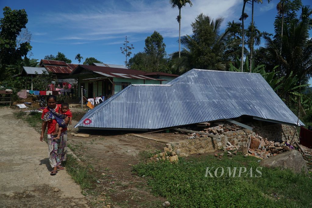 Warga melintas di depan rumah ambruk akibat gempa di Jorong Timbo Abu, Nagari Kajai, Kecamatan Talamau, Pasaman Barat, Sumatera Barat, Sabtu (12/3/2022). Jorong Timbo Abu adalah pusat gempa M 6,1 pada Jumat (25/2/2022) dan paling parah terdampak gempa. 
