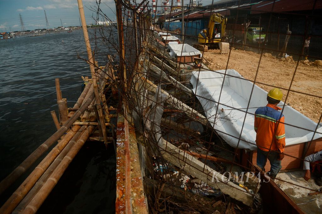 Pekerja berada di balik tembok pembatas tengah menyiapkan konstruksi untuk menguatkan tembok yang juga berfungsi sebagai tanggul laut. Tampak permukaan laut (kiri) yang lebih tinggi dari daratan kawasan berikat Pelabuhan Tanjung Emas Kota Semarang, Jawa Tengah, yang berada di sebelah kanan tembok, Jumat (3/6/2022). 