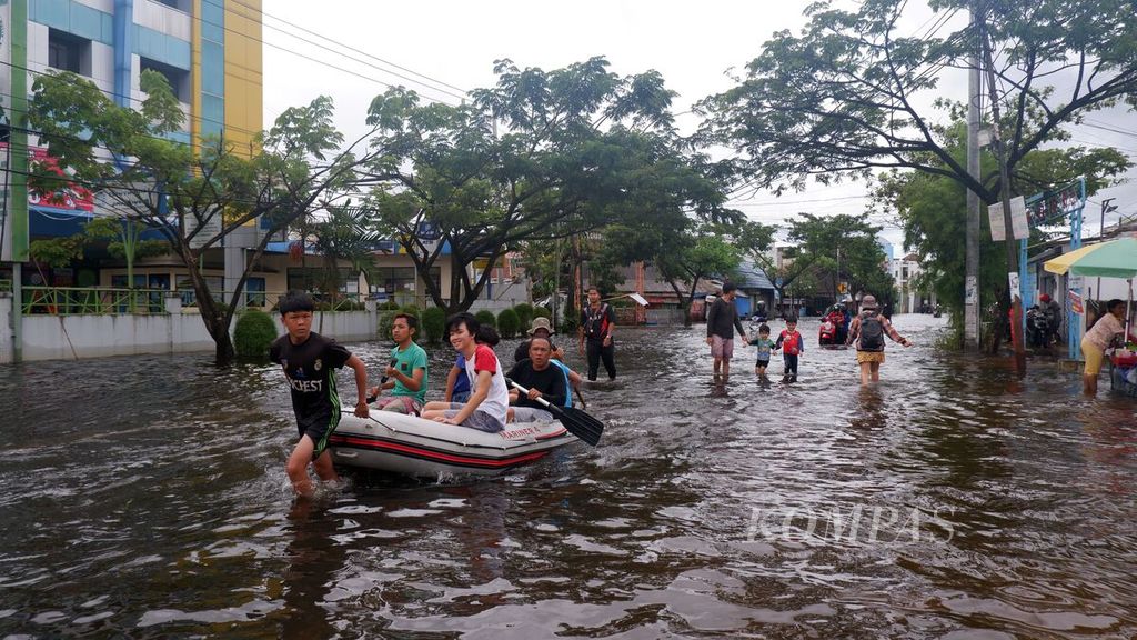 Warga melintasi Jalan Pramuka, salah satu jalan protokol di Kota Banjarmasin, Kalimantan Selatan, dengan menggunakan perahu karet, Sabtu (16/1/2021). Jalan itu juga terendam pada hari ketiga banjir di Kalsel.