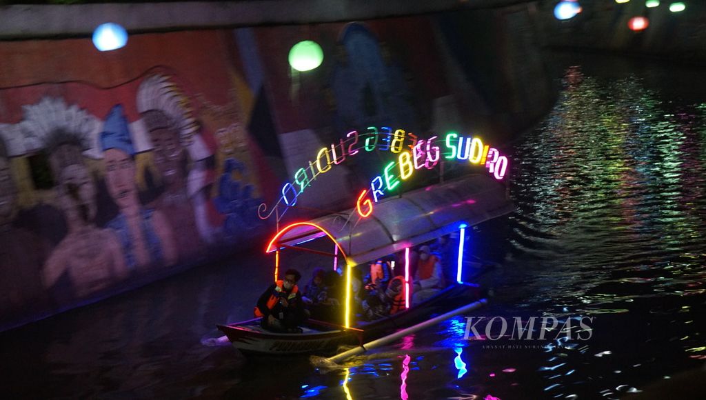Perahu berhiaskan lampu warna-warni melintasi Kali Pepe dalam Grebeg Sudiro, di Kota Surakarta, Jawa Tengah, Senin (16/1/2023) malam. Keberadaan wisata perahu membangkitkan ingatan tentang kejayaan jalur transportasi air di kota tersebut pada masa lampau.