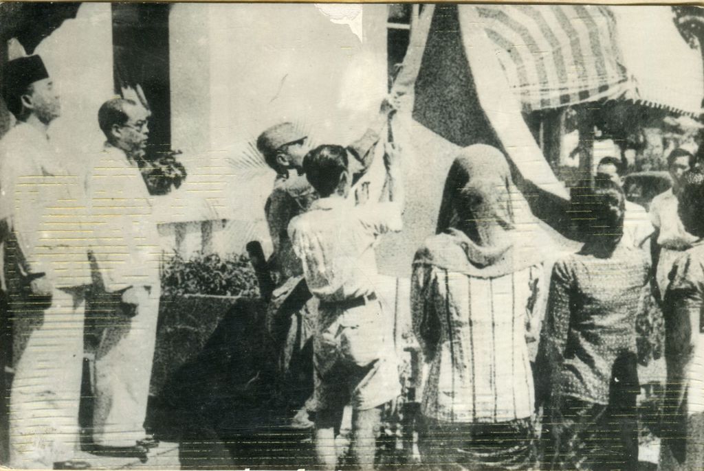 Upacara penaikan bendera Sang Merah Putih di halaman Gedung Pegangsaan Timur 56 (Gedung Proklamasi). Tampak antara lain Soekarno, Hatta, Latief Hendraningrat (menaikkan bendera), Ny. Fatmawati Soekarno dan Ny. SK Trimurti.
