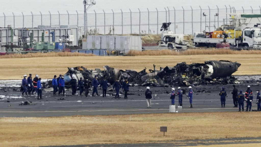 Polisi dan pemadam kebakaran berkumpul di sekitar pesawat Penjaga Pantai Jepang yang terbakar di Bandara Haneda, Rabu (3/1/2023). Pejabat transportasi dan polisi memulai penyelidikan di lokasi.