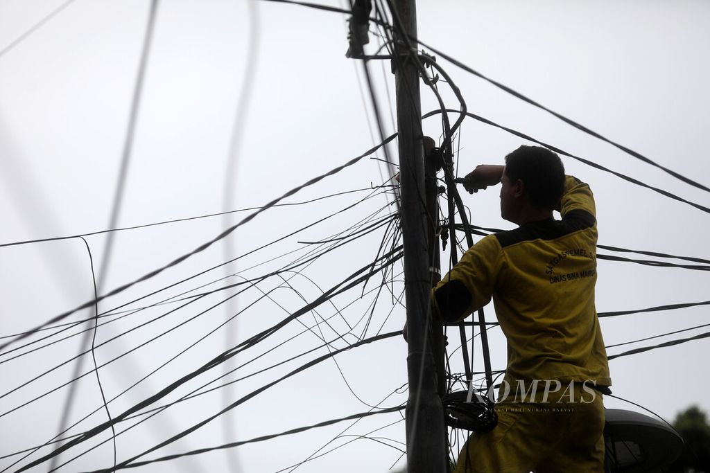 Petugas dinas bina marga memotong kabel utilitas yang dibersihkan dari tiang-tiang di kawasan Tebet, Jakarta, Selasa (3/1/2023).