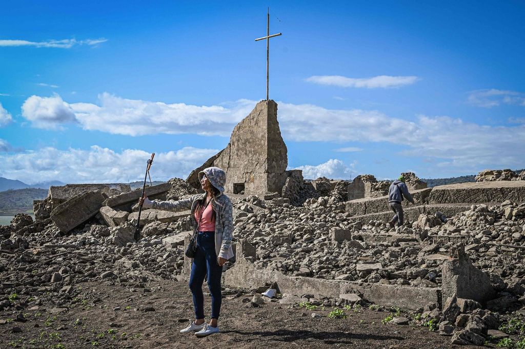 Seorang perempuan mengambil foto di dekat reruntuhan gereja di kota tua Pantabangan, Provinsi Nueva Ecija, pada 26 April 2024. Sisa-sisa kota tua Pantabangan kembali muncul di kawasan utara Filipina setelah permukaan air bendungan turun di tengah kekeringan yang melanda sejumlah negara. 