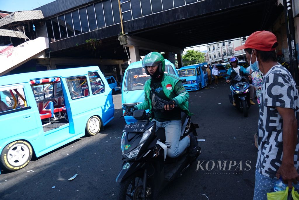 Seorang pengemudi ojek daring melintas di dekat antrean mikrolet alias mikro jurusan Pasar 45-Tuminting yang mengantre panjang di kawasan Pasar 45, Manado, Sulawesi Utara, Selasa (9/5/2023).