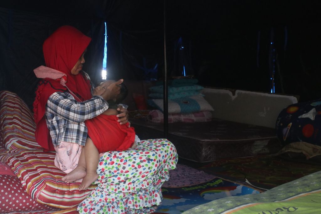 Salah satu warga menidurkan anaknya di dalam tenda darurat, Kampung Sedong Kulon, Kelurahan Bojongherang, Kecamatan Cianjur, Kabupaten Cianjur, Jawa Barat, Sabtu (21/1/2023). Di wilayah ini sebanyak 13 rumah rusak berat dan puluhan jiwa terpaksa tinggal di tenda-tenda pengungsian.