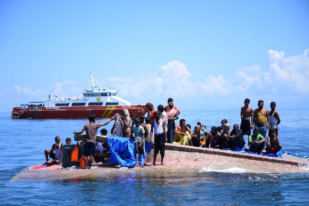 Para pengungsi Rohingya berdiri di atas perahu mereka yang terbalik, menunggu dievakuasi petugas Basarnas di perairan sekitar 29 kilometer di sebelah barat pantai Aceh, Kamis (21/3/2024). 