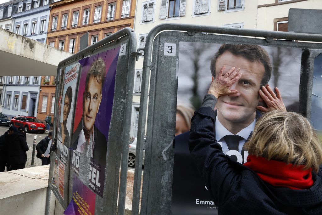 Seorang perempuan menyentuh poster kampanye Presiden Perancis Emmanuel Macron dalam putaran pertama pemilu Presiden Perancis di Strasbourg, Perancis timur, Minggu (10/4/2022). 