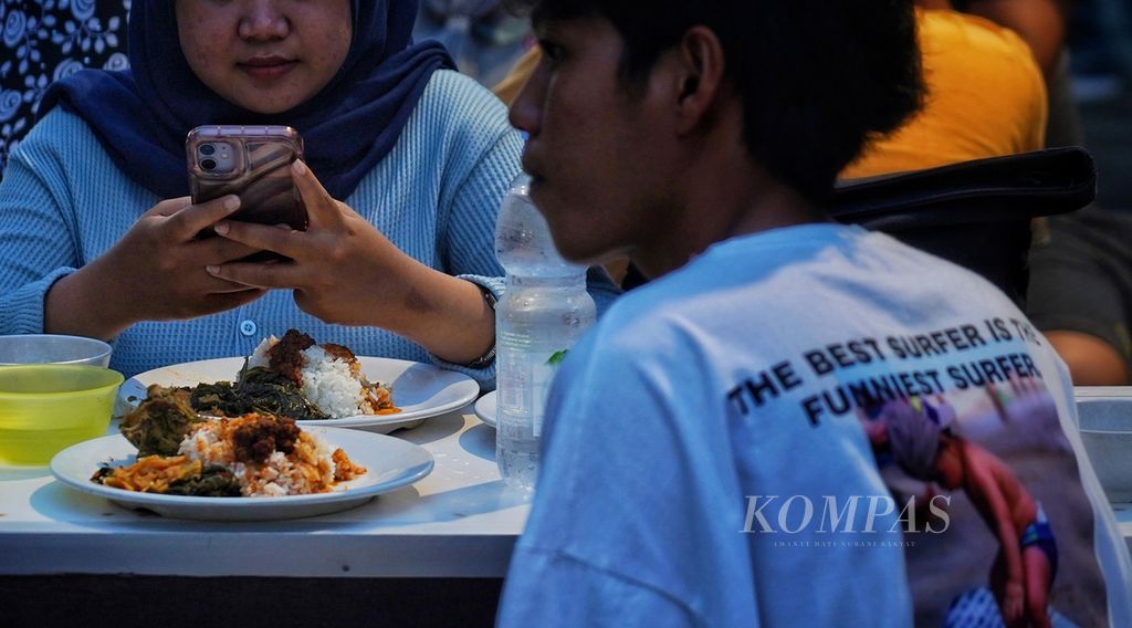 Seorang warga mengisi waktu dengan bermain gawai saat menunggu waktu buka puasa di sentra pedagang nasi kapau kawasan Senen, Jakarta, Rabu (13/3/2024). 