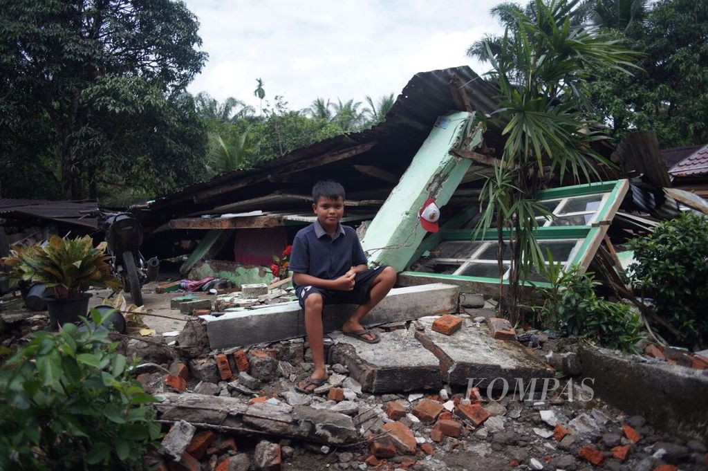 Ghalib (11) tengah menunggu orangtua di depan rumahnya yang runtuh di Nagari Kajai, Kecamatan Talamau, Kabupaten Pasaman Barat, Sumatera Barat, Sabtu (26/2/2022). Pasaman Barat dan sekitarnya dilanda gempa bermagnitudo 6,1 pada 25 Februari lalu.