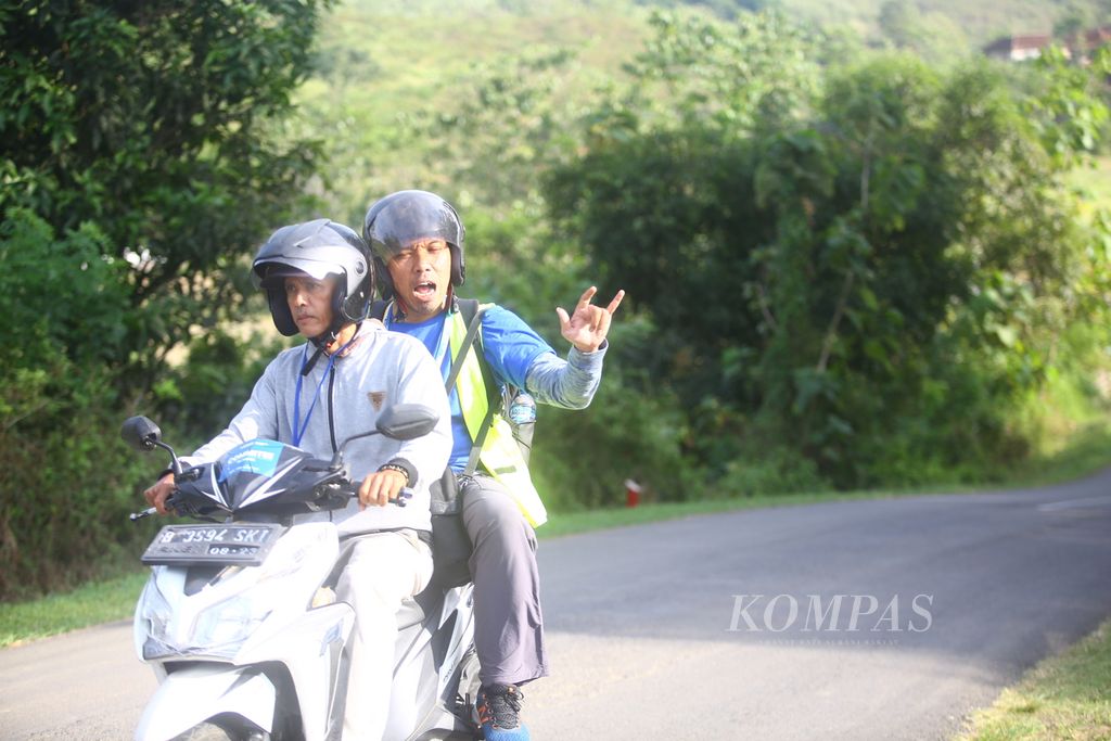 Pewarta foto harian <i>Kompas</i>, Hendra A Setyawan, melambaikan tangan saat membonceng tukang ojek yang mengantarnya melintasi etape ke-1 Cycling de Jabar sejauh 199,7 km dari Ciletuh, Sukabumi, hingga Ranca Buaya, Garut, Jawa Barat, Minggu (8/7/2023).