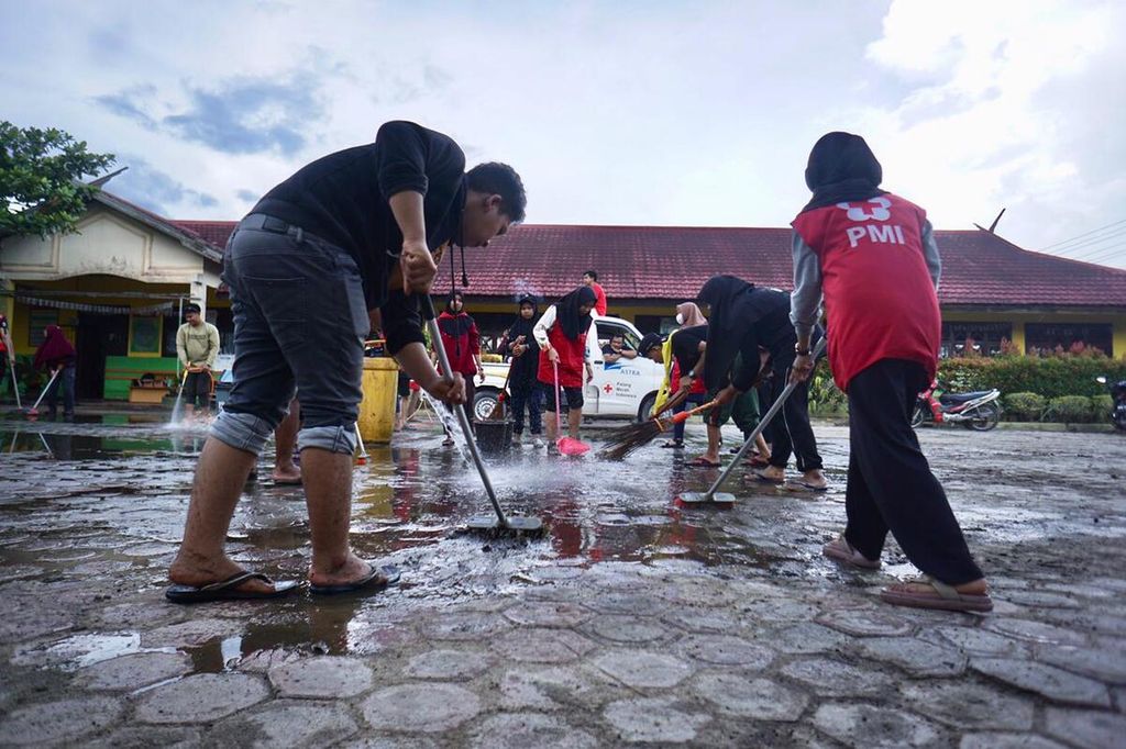 Sukarelawan dari Palang Merah Indonesia, warga, dan anak-anak sekolah mulai membersihkan lingkungan sekolah yang lebih dari sebulan direndam banjir, Minggu 6/11/2022).