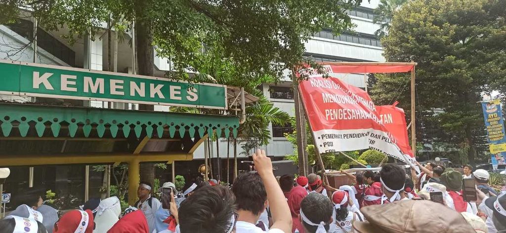 Sejumlah peserta aksi damai yang terdiri dari tenaga kesehatan dan tenaga medis mencoba menurunkan spanduk yang bertuliskan dukungan terhadap RUU Kesehatan yang dipasang di depan kantor Kementerian Kesehatan di Jakarta, Senin (8/5/2023). 